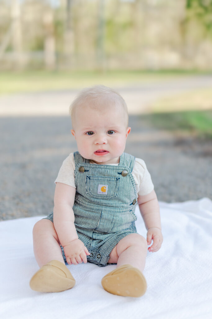 Baby giggling with a bright smile while sitting in the grass during their milestone session.