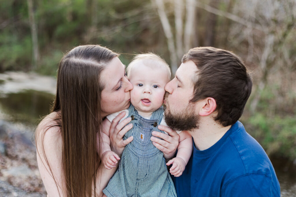 Mom and dad kissing each cheek together while holding their baby during the spring milestone session.
