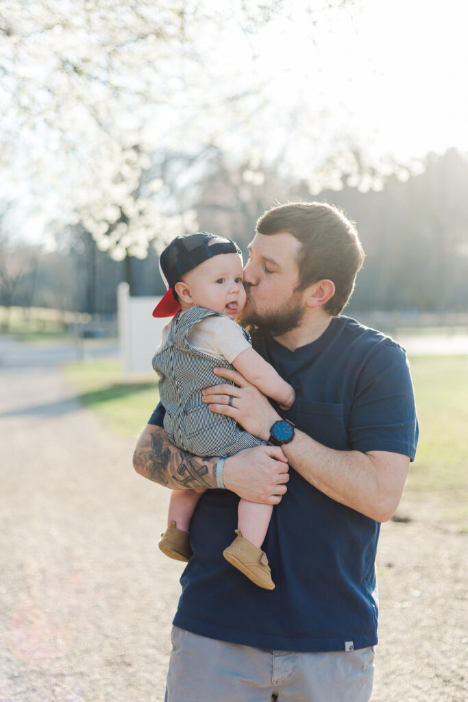 Dad kissing baby’s cheek, capturing a tender moment in the springtime session.