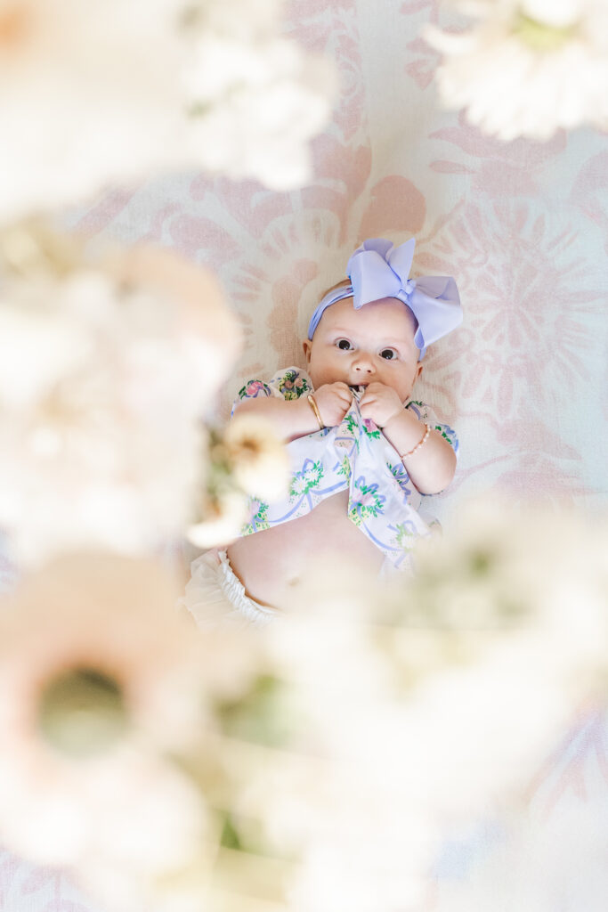 little girl laying on blanket looking up through flower mobile at the camera
