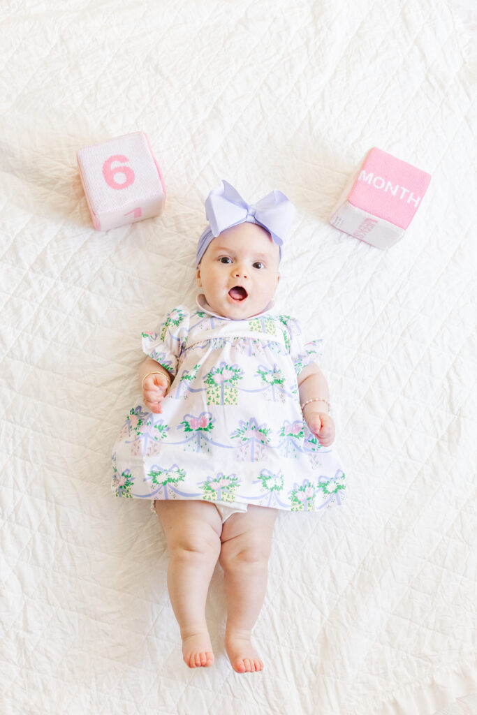 Little girl laying on white quilted blanket with quilted blocks with "6 and months" embroidered on them during 6 month milestone session with 5U Photography 