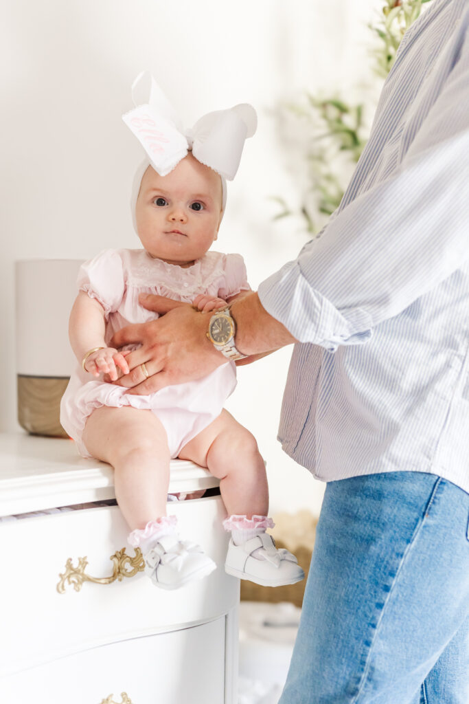 Ella sitting on edge of her white dresser with dad's help during 6 month milestone session