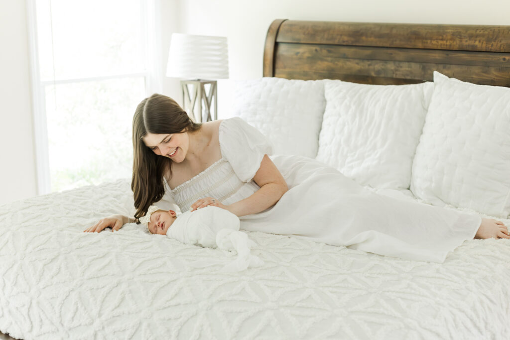 Mom laying next to Eleanor on the bed, touching looking down at her newborn baby girl, and smiling softly.