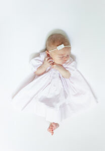 classic heirloom picture of newborn baby girl laying in Feltman Brother's gown on white backdrop during newborn session with 5U Photography
