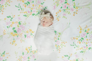 baby girl lying on delicate floral backdrop in white swaddle with cream bow sleeping peacefully