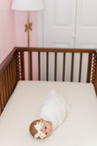 baby girl in white swaddle laying on changing table in pink nursery during in-home newborn session with 5uphotography