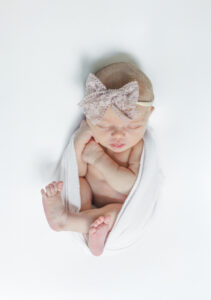 Eleanor swaddled and posed on a creamy white backdrop, photographed using a portable studio setup.