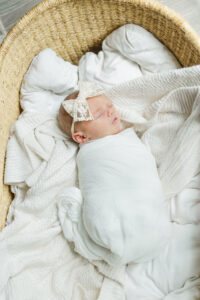 Overhead shot of Eleanor asleep in a woven basket with a soft pink wrap and neutral knit textures during in-home newborn session with 5U Photography