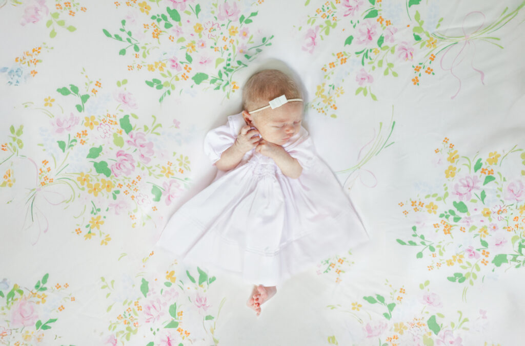Baby Eleanor in a classic pink Feltman Brothers gown, resting on a light and airy floral backdrop with beautiful bow details during in-home newborn session with 5U Photography