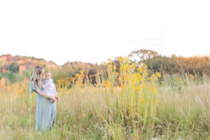 Mother in a flowy client closet gown and denim jacket holding her baby while the rest of the family coordinates in earthy neutrals during fall photo session