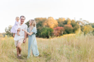 Family walking through a field at sunset wearing coordinated camel, cream, and sage green outfits styled with cable knit sweaters and boots for their fall family photos in birmingham alabama with 5U Photography