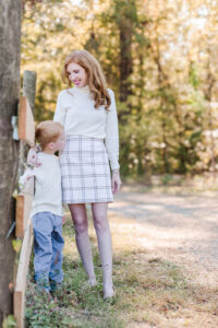 Mom looking down at son standing by fence at Old Baker Farm using styling tips for fall family photos with light neutrals and beautiful textured fabrics