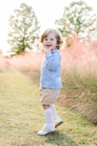 Little boy standing in fall styled outfit surrounded by purple grasses at Railroad Park in Birmingham AL during photo session with 5U Photography 