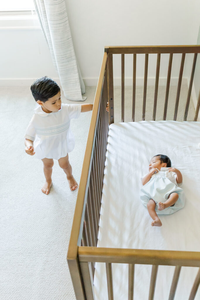 Toddler big brother standing by baby brother’s crib during an in-home newborn session in Trussville, Alabama by 5U Photography.