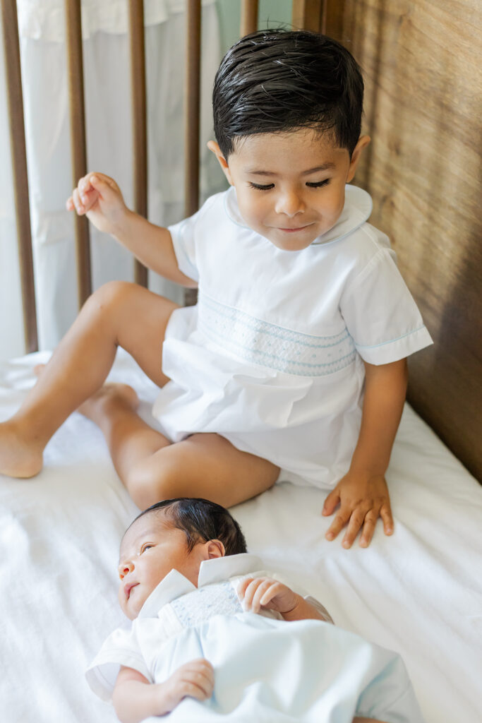 Big brother sitting sweetly in the crib with newborn baby brother during a Trussville, Alabama in-home newborn photography session.