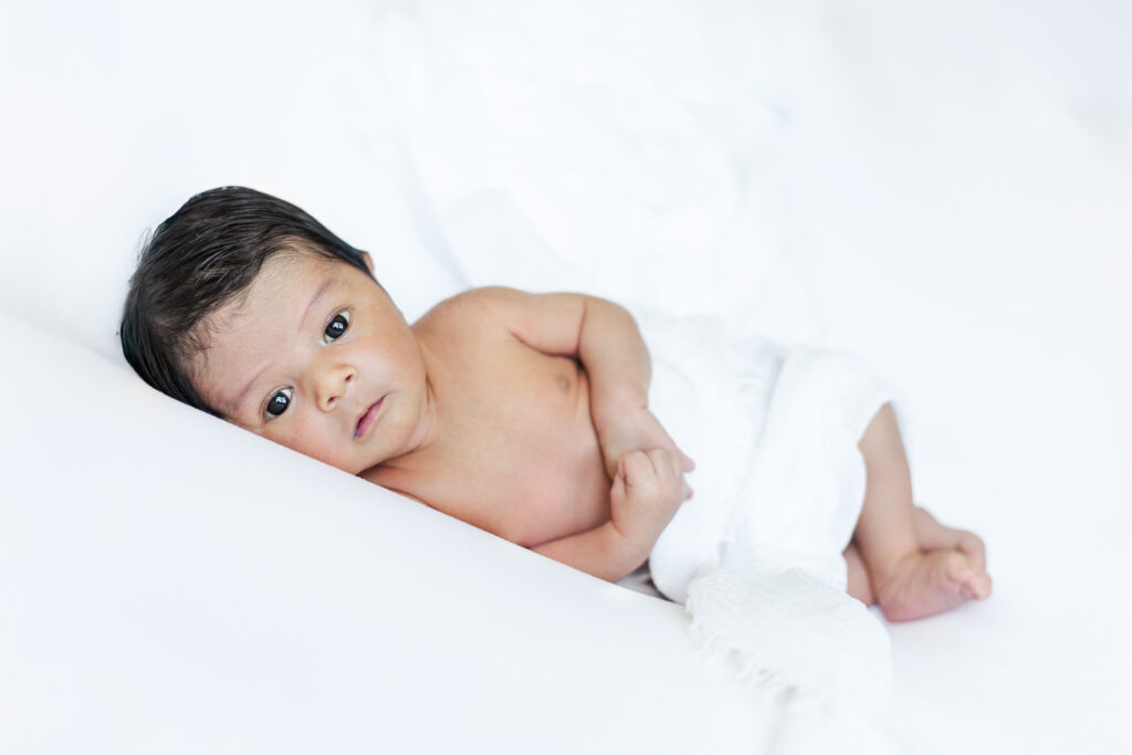 Close-up portrait of newborn baby boy swaddled on a white blanket during an in-home newborn photography session in Trussville, Alabama.