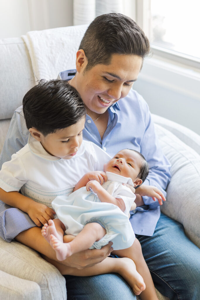 Father holding toddler and newborn baby together in a cozy chair during an in-home newborn session in Trussville, Alabama.