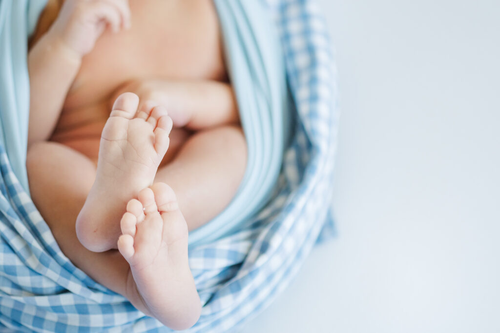Detail photo of newborn baby’s tiny feet wrapped in blue gingham blanket during a Trussville, Alabama lifestyle newborn session.