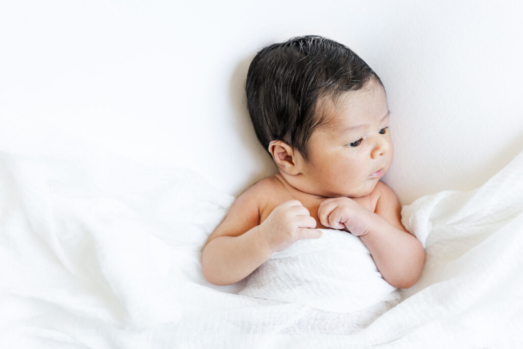 Close-up of newborn baby boy wrapped in a soft white blanket on bed during a Trussville, Alabama in-home newborn photography session.
