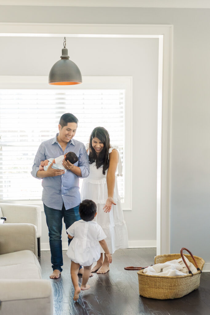 Toddler running toward parents holding newborn baby in their living room during a Birmingham and Trussville in-home newborn session.